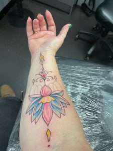 Ladies forearm lotus flower tattoo coloured in blue pink and yellow