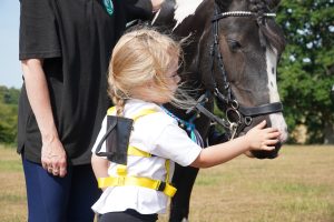 Black & white pony being stroked on the nose by a young girl in white t shirt with blonde hair