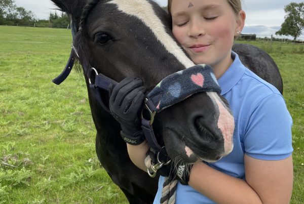 a young lady wearing a light blue tshirt holding her face to her pony's face.