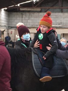 Child wearing Equihandee Core Support during equine therapy session being supported by a helper or parent